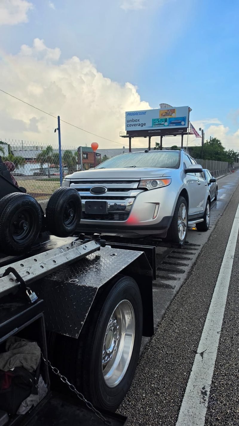 Ford Edge plateado cargado en la plataforma de la grúa al costado de una autopista de Miami